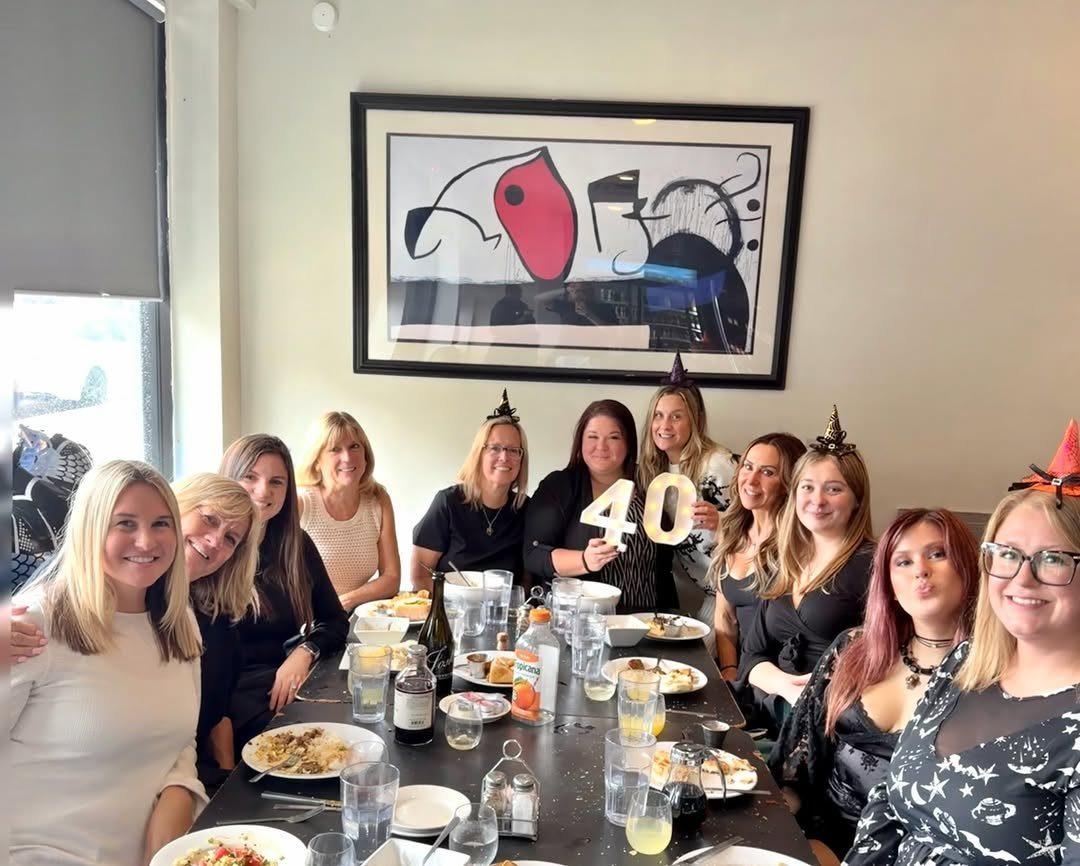 Group of women celebrating a 40th birthday with food and drinks at a table.