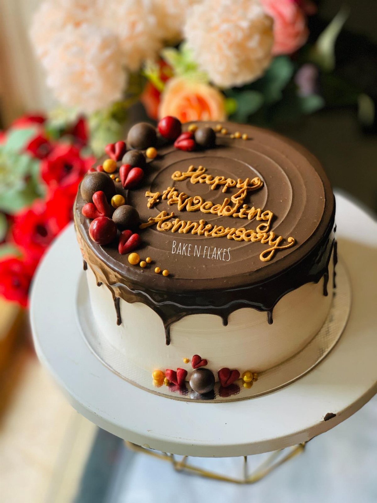 Chocolate drip anniversary cake decorated with berries, chocolate spheres, and gold lettering.