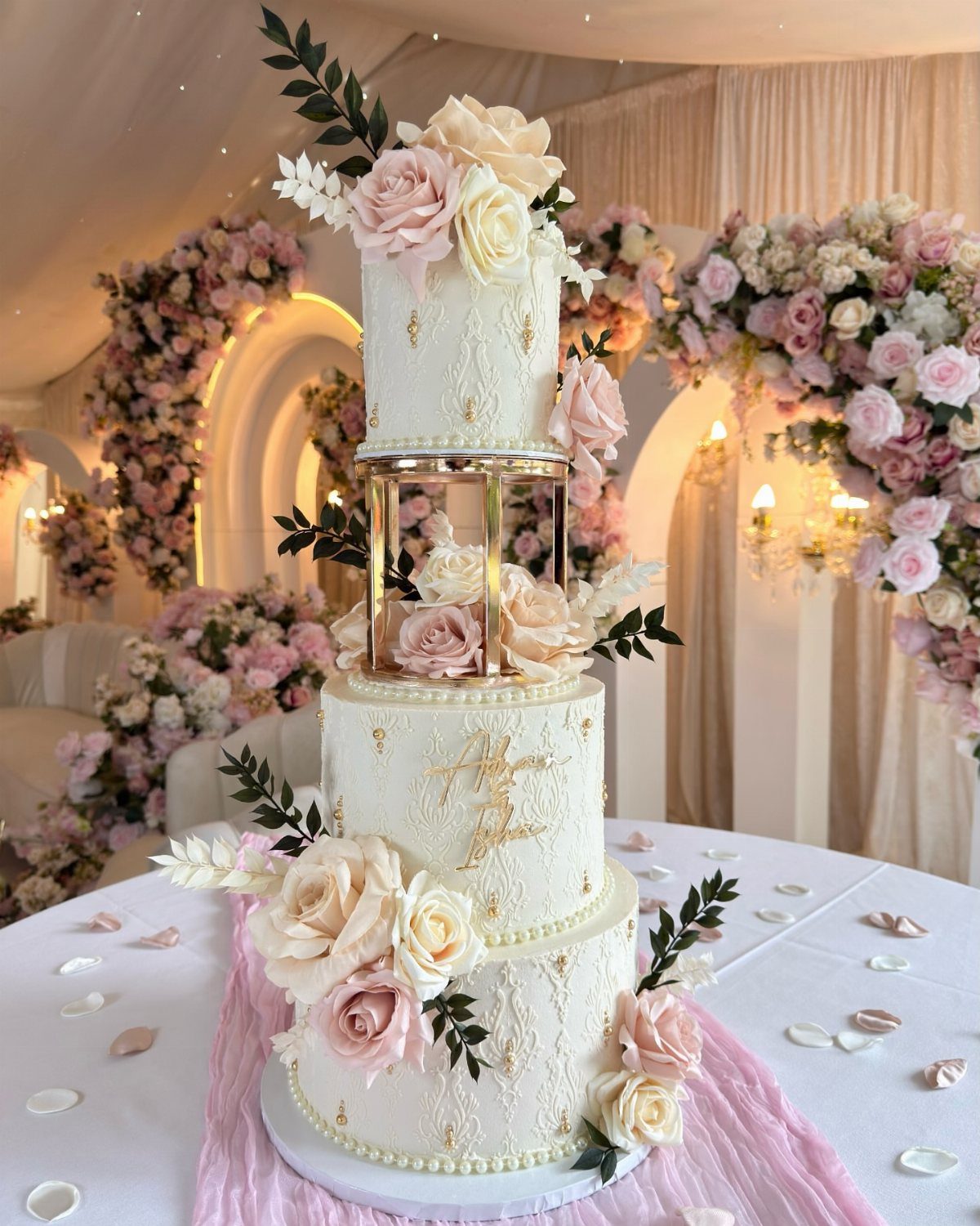 Three-tier white anniversary cake with gold pillars and pale pink rose decorations
