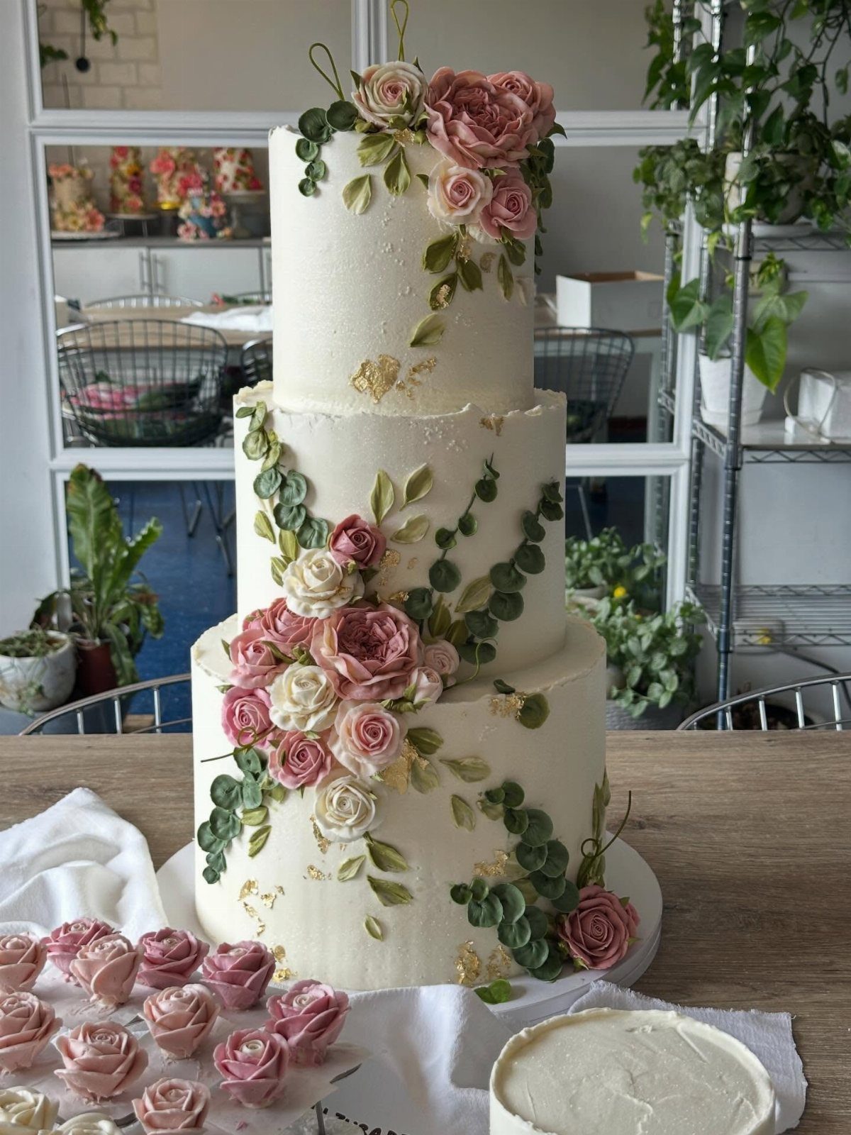 Three-tier white cake decorated with pink and cream roses and green leaves.