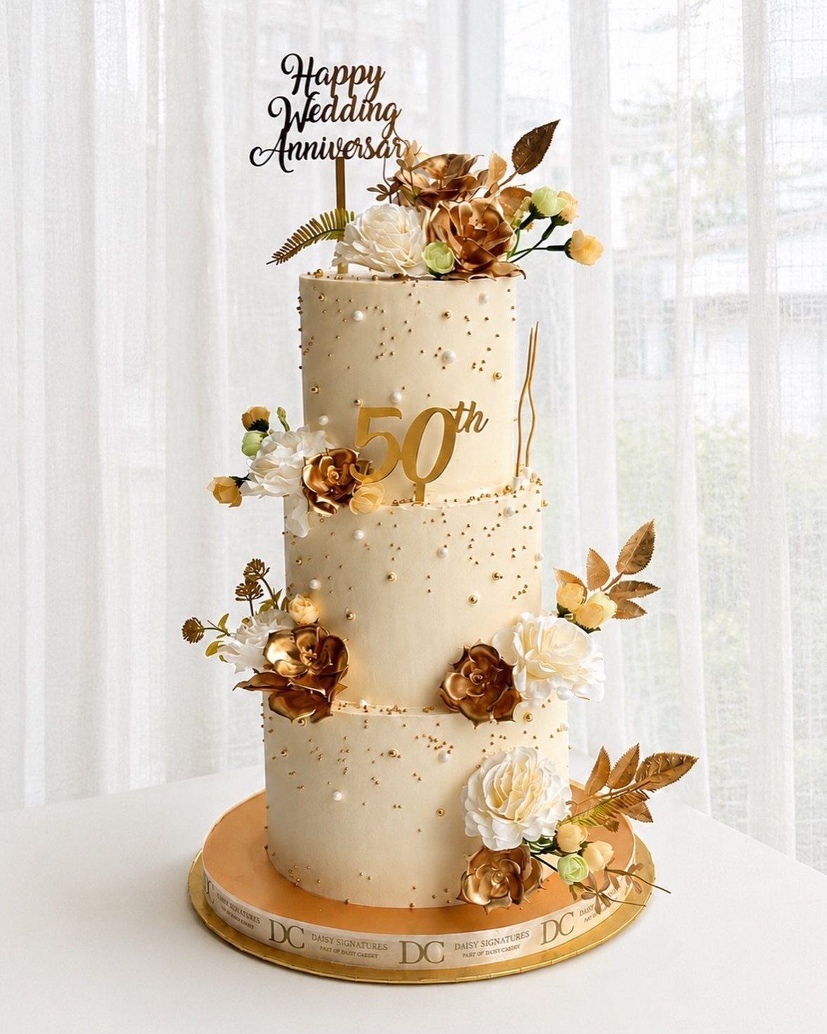 Three-tier white anniversary cake with gold flowers and a gold 50th topper