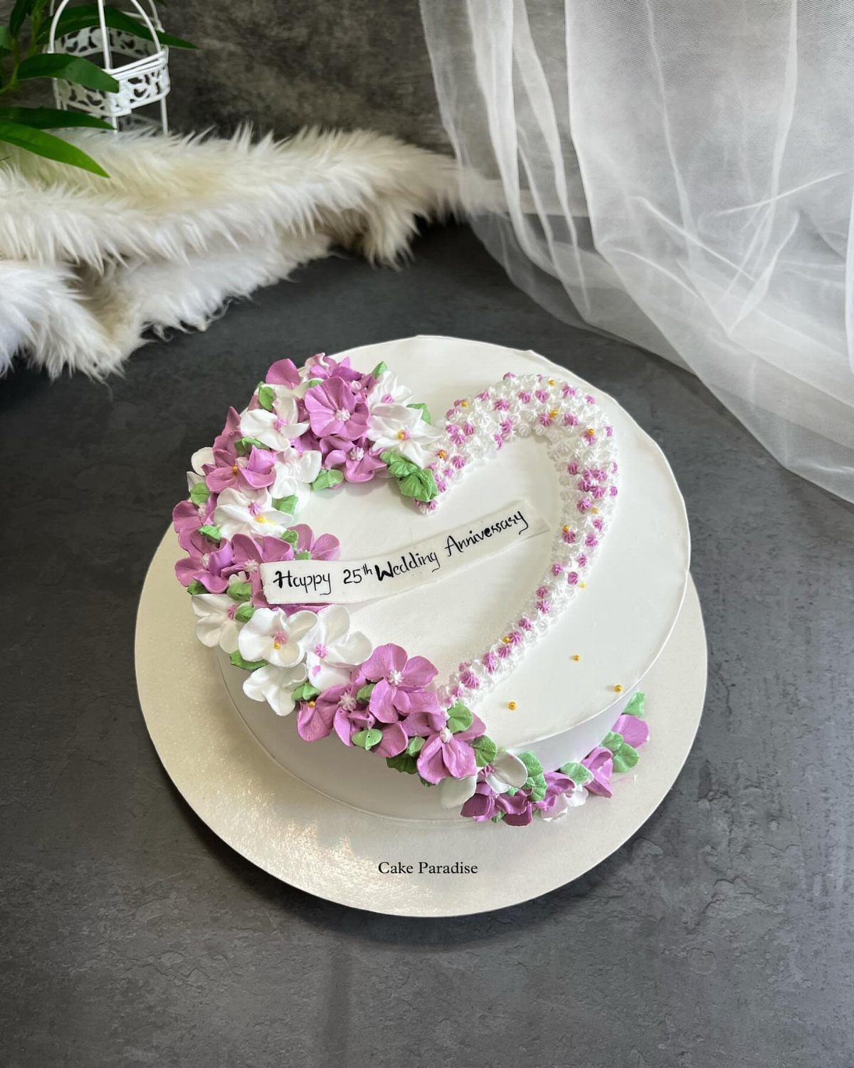 White anniversary cake decorated with a heart of purple and white buttercream flowers.