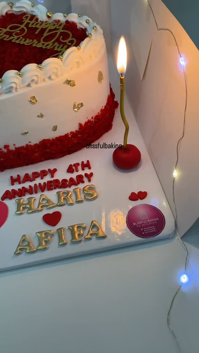 White frosted red velvet anniversary cake with gold lettering and a lit candle