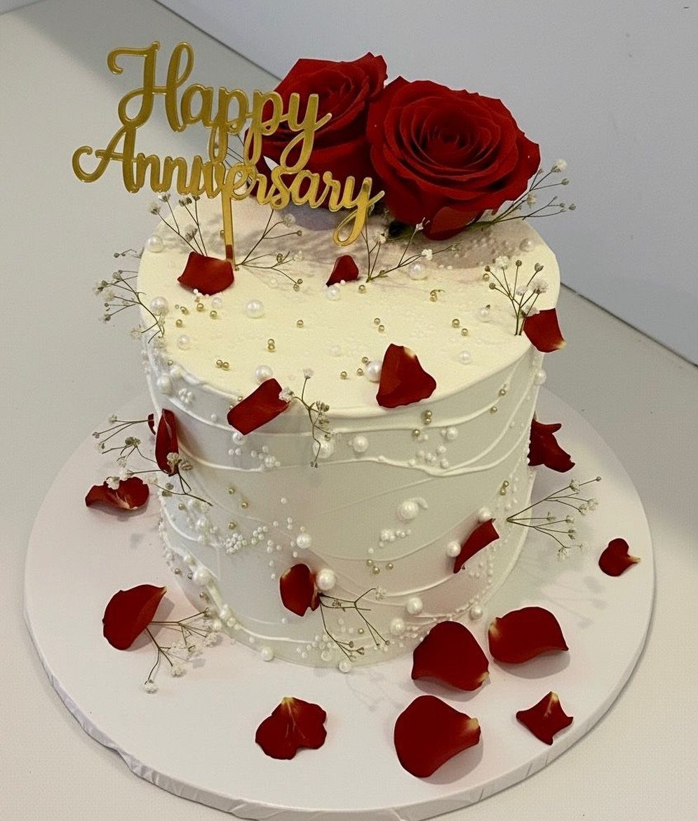 White frosted anniversary cake topped with red roses and a gold topper.