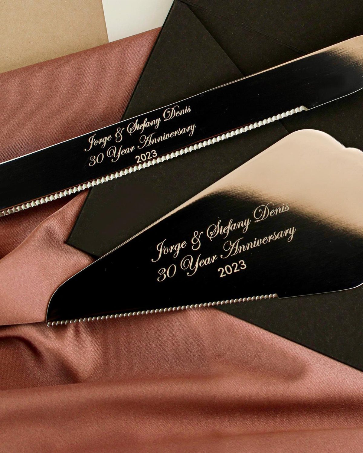 Black metal cake servers engraved with a 30th wedding anniversary message on satin fabric