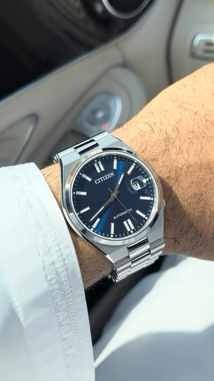Silver Citizen automatic watch with blue dial on a man's wrist in a car