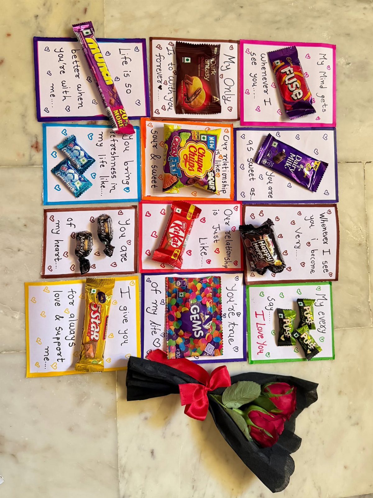 Handmade romantic candy cards and red roses arranged on a white marble surface.