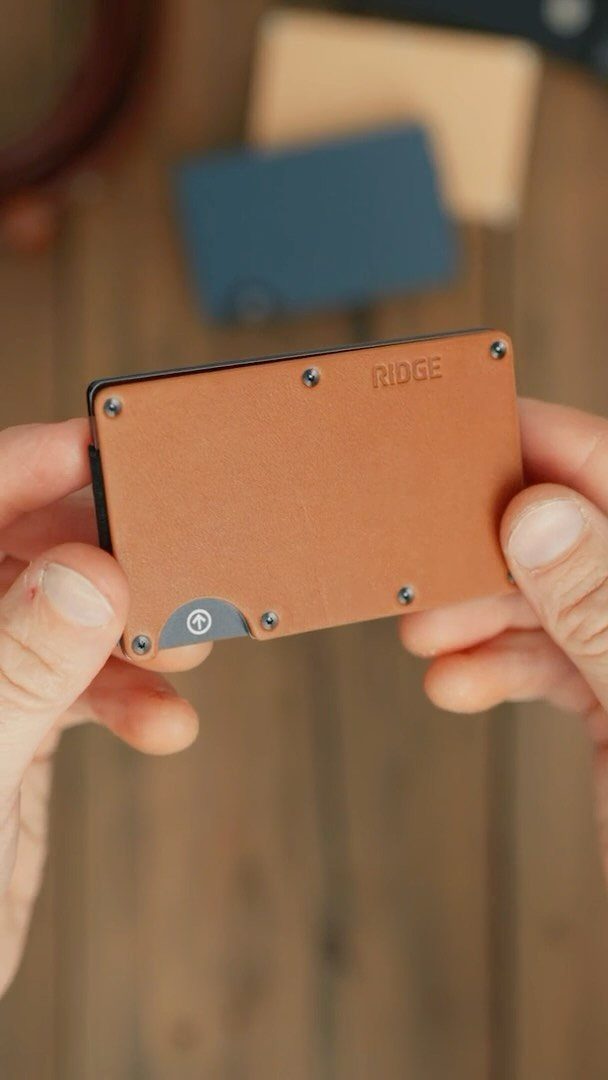 Brown leather Ridge minimalist wallet held by hands over a wooden background