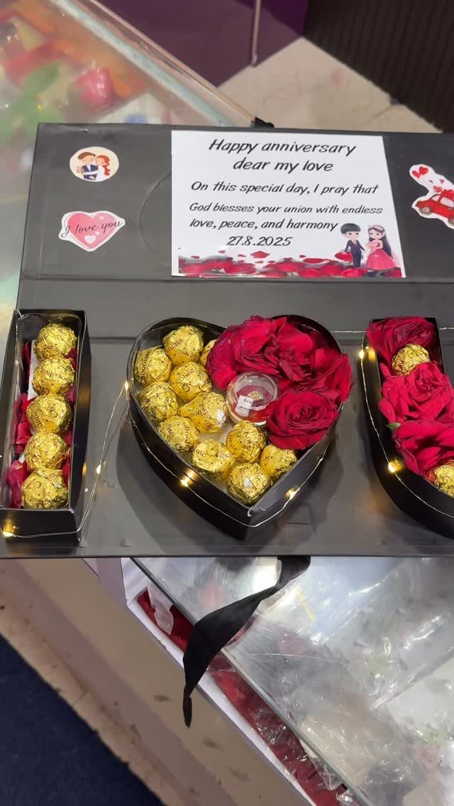 Heart-shaped arrangement of gold chocolates and red roses in a black gift box