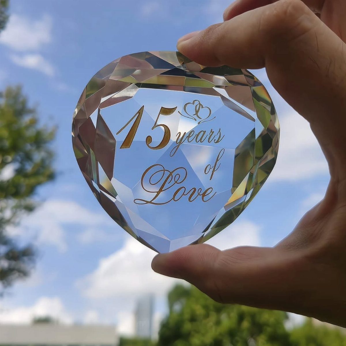 Heart-shaped crystal ornament engraved with 15 years of Love held against blue sky