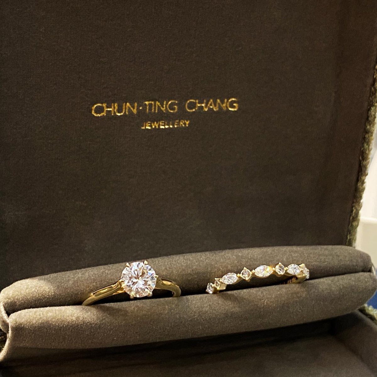 Two gold diamond rings resting inside a dark olive green velvet jewelry box.