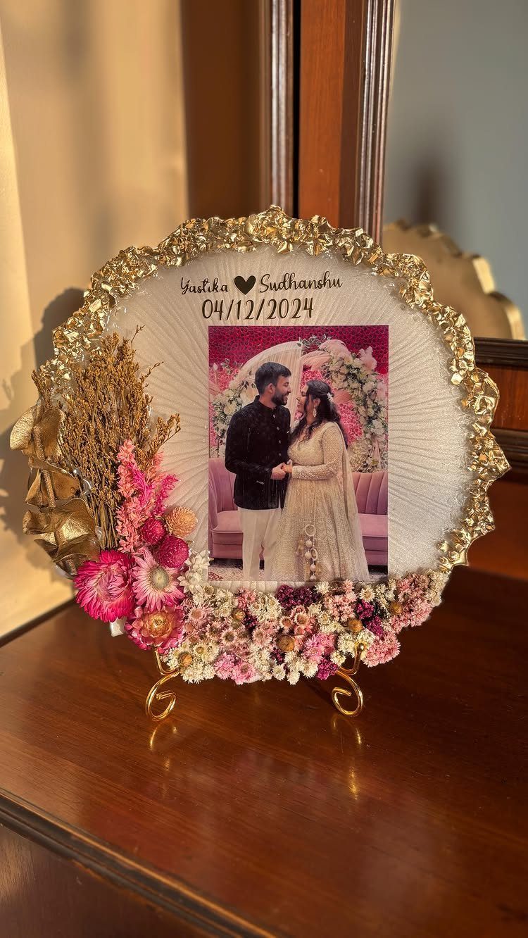 Circular gold framed couple's photo decorated with pink and white dried flowers.