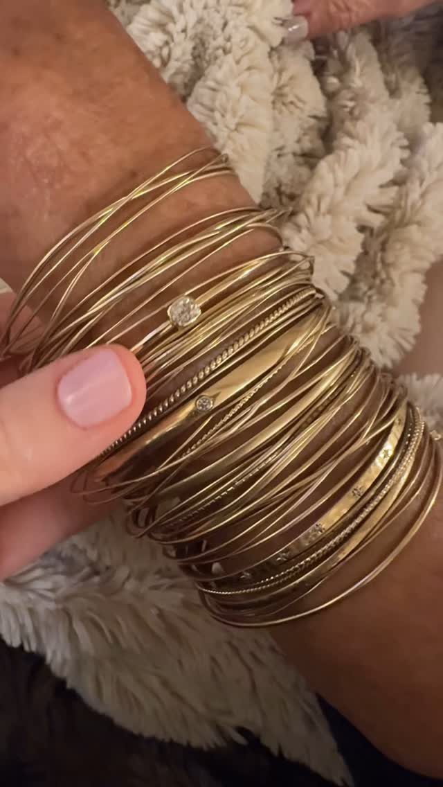 Stack of gold bangles and bracelets on a wrist with pink nails