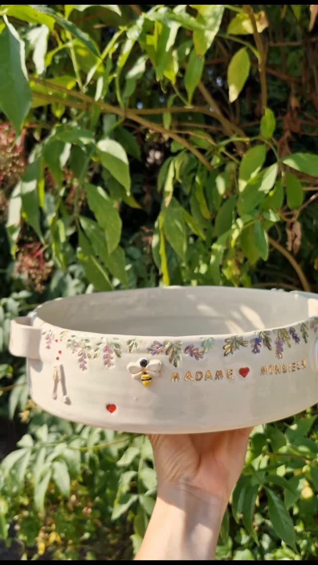White ceramic pottery bowl with floral designs and a bee held outdoors.