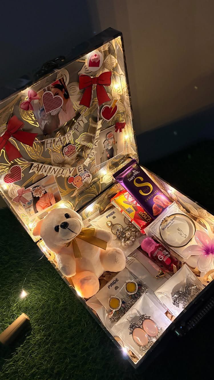 Open suitcase filled with anniversary gifts, teddy bear, jewelry, and fairy lights.